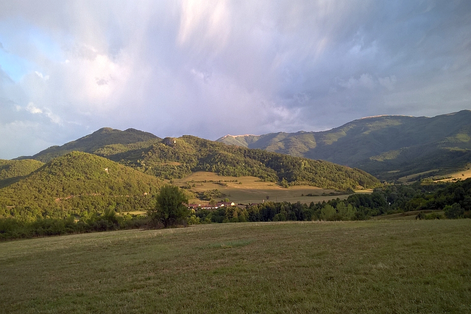 Rolling Green Hills And Mountains Under A Partly Cloudy Sky